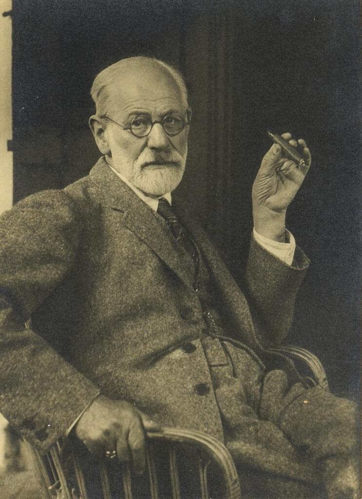 Retrato em preto e branco de Sigmund Freud sentado e segurando um charuto