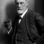 Retrato em preto e branco de Sigmund Freud sentado, usando terno e segurando um charuto